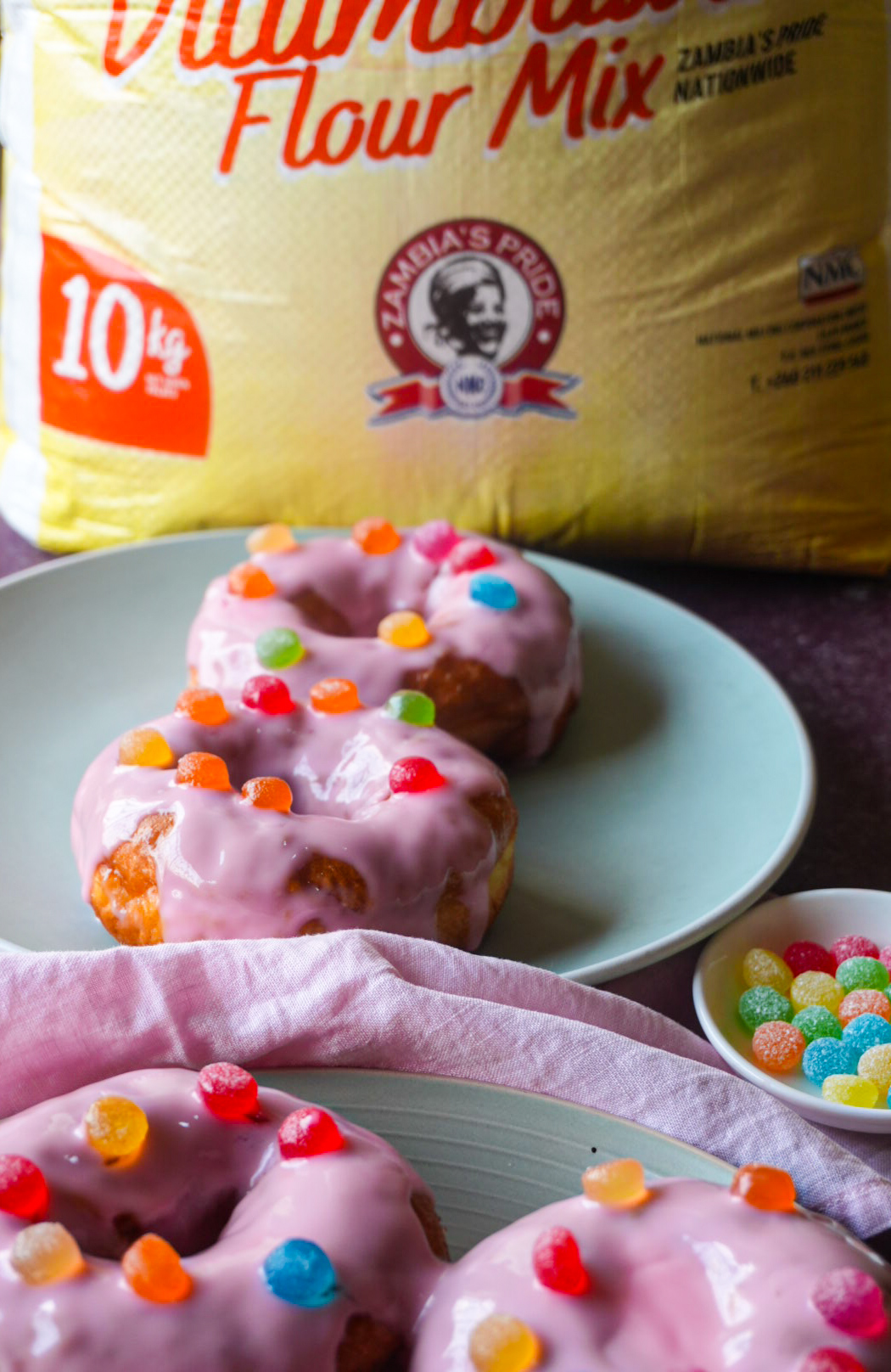 Pink glazed doughnuts decorated with colourful gum drops, styled with Zambia's Pride flour packaging